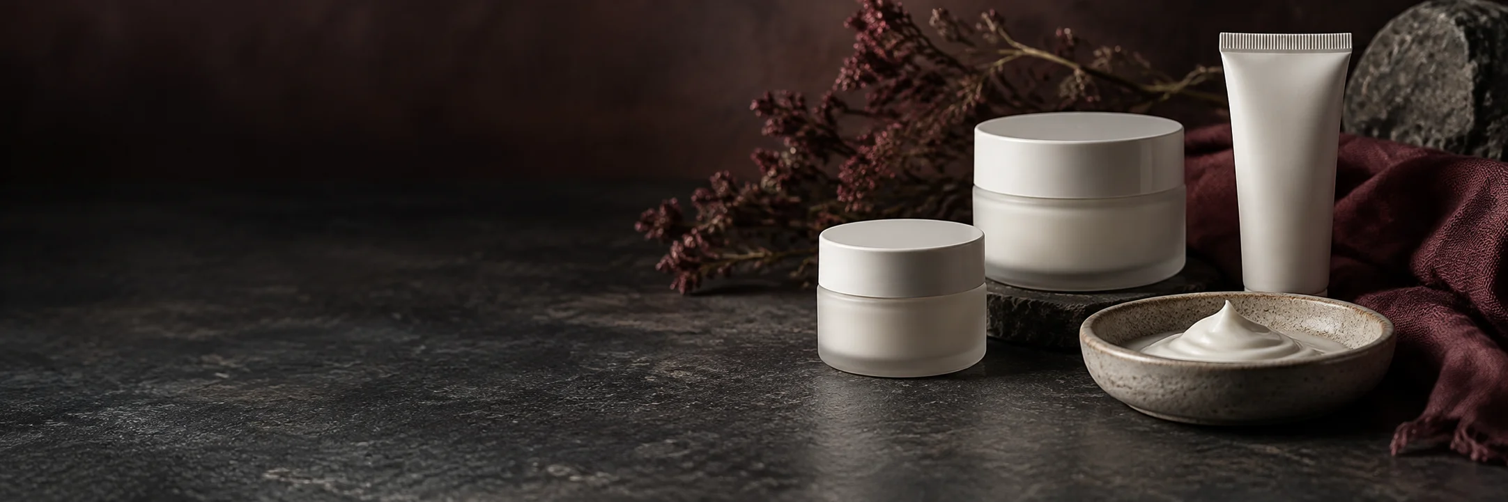 Two unmarked cosmetic cream jars, a squeeze tube and a dish of white cream illustrating cannabis topicals product-format context.