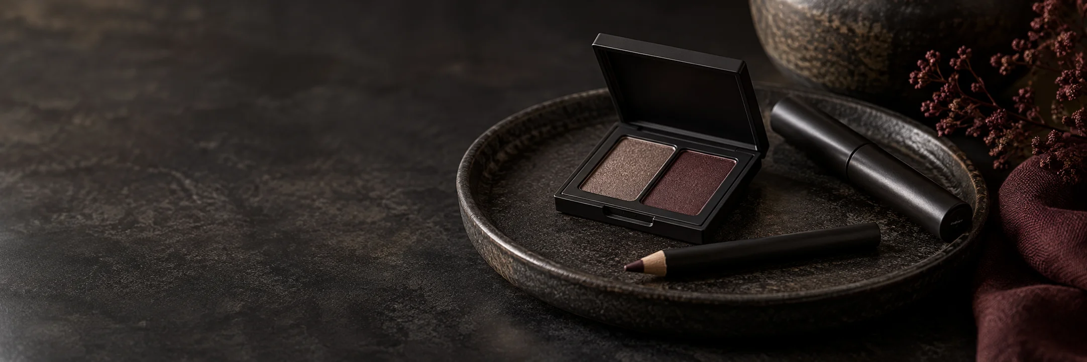 An open muted eyeshadow compact, a plain mascara-style tube and an unmarked cosmetic pencil illustrating traditional eye cosmetics product-format context.