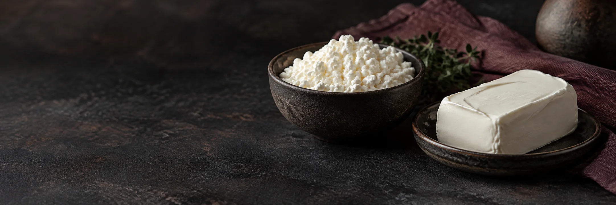 A bowl of loose white cheese curds and a smooth white fresh-cheese block illustrating cottage cheese ingredient context.