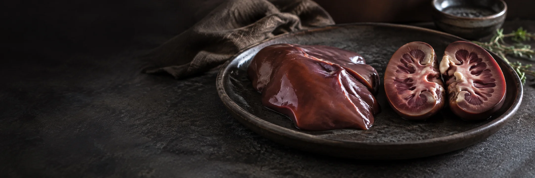 Separate raw liver and halved kidney portions on a dark ceramic tray illustrating Baptista 2024 game-organ elemental study research context.