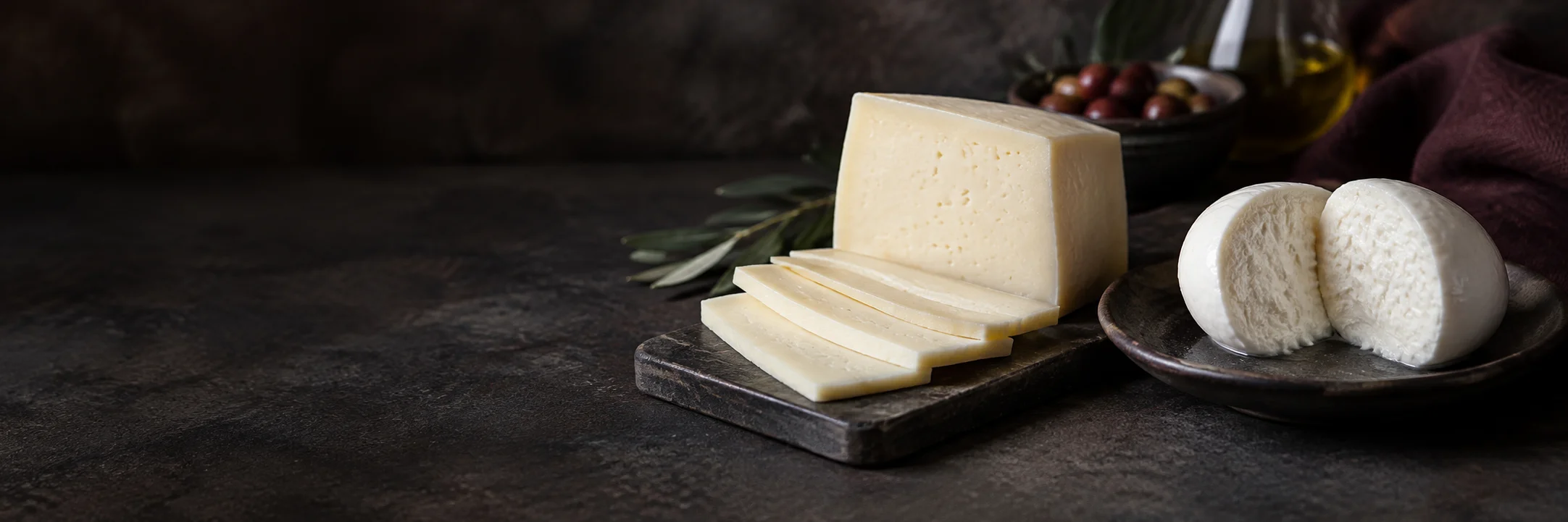 A pale semi-firm cheese block and slices beside a cut white mozzarella ball illustrating dairy cheese product-format context.
