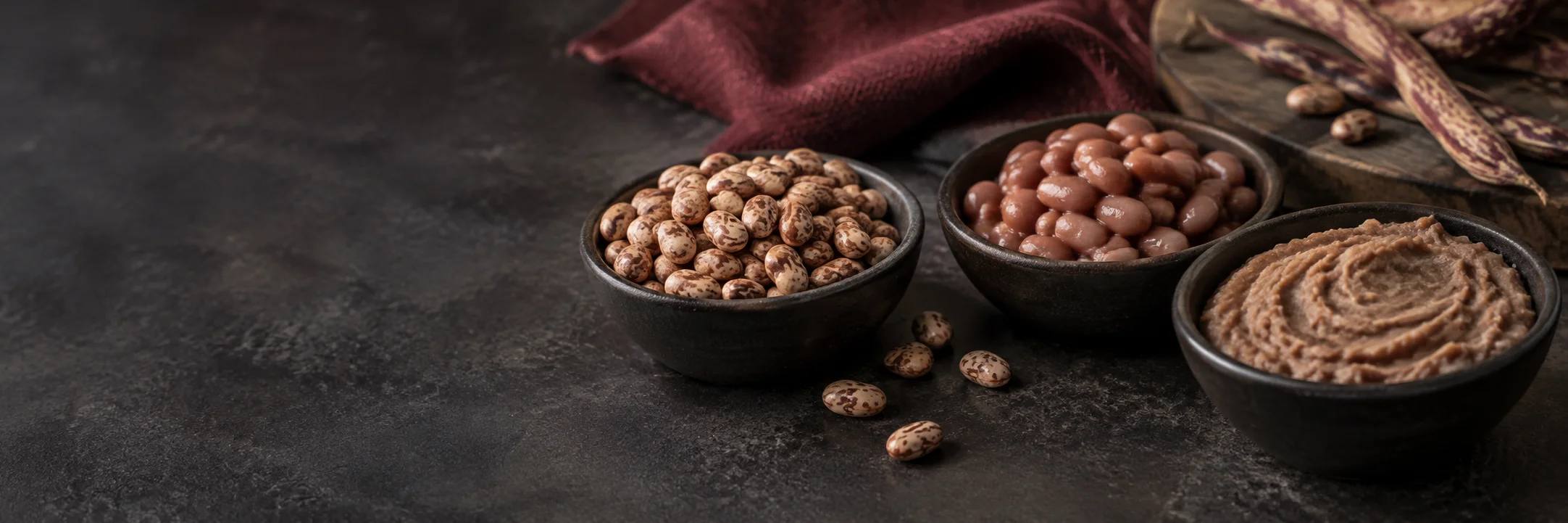 Separate dishes of dry pinto beans, cooked pinto beans and smooth mashed beans illustrating refried beans ingredient context.