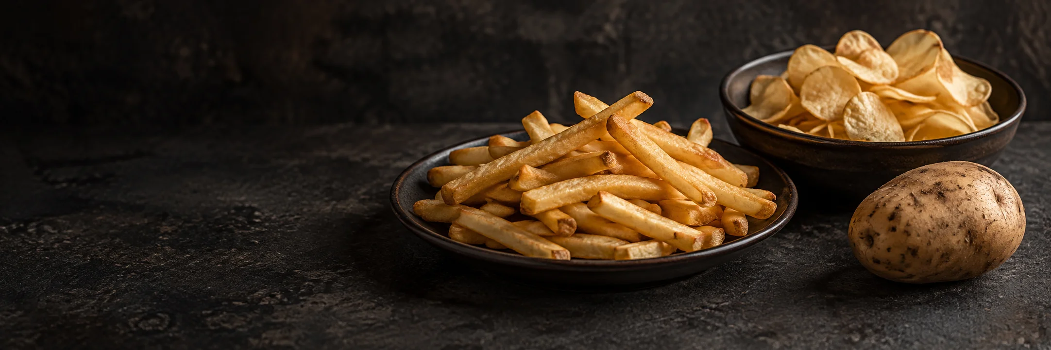 Separate dishes of golden French fries and thin potato chips beside an unpeeled potato illustrating french fries ingredient context.