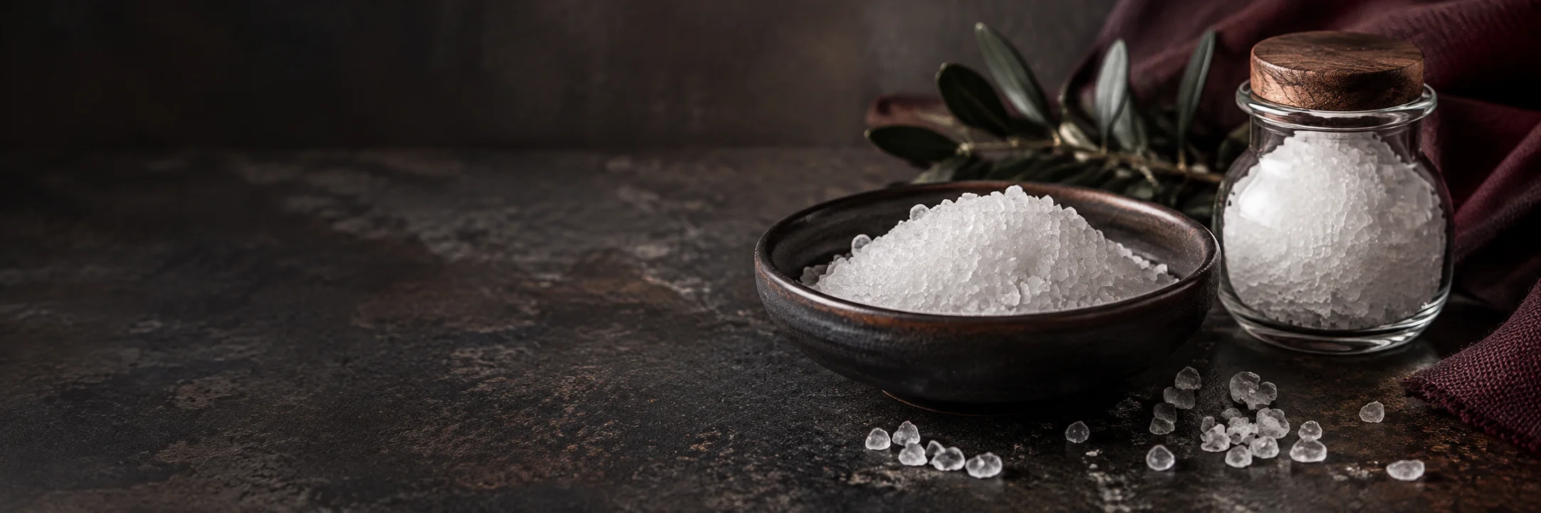White salt crystals in a dark dish and an unmarked glass container illustrating sea salt ingredient context.
